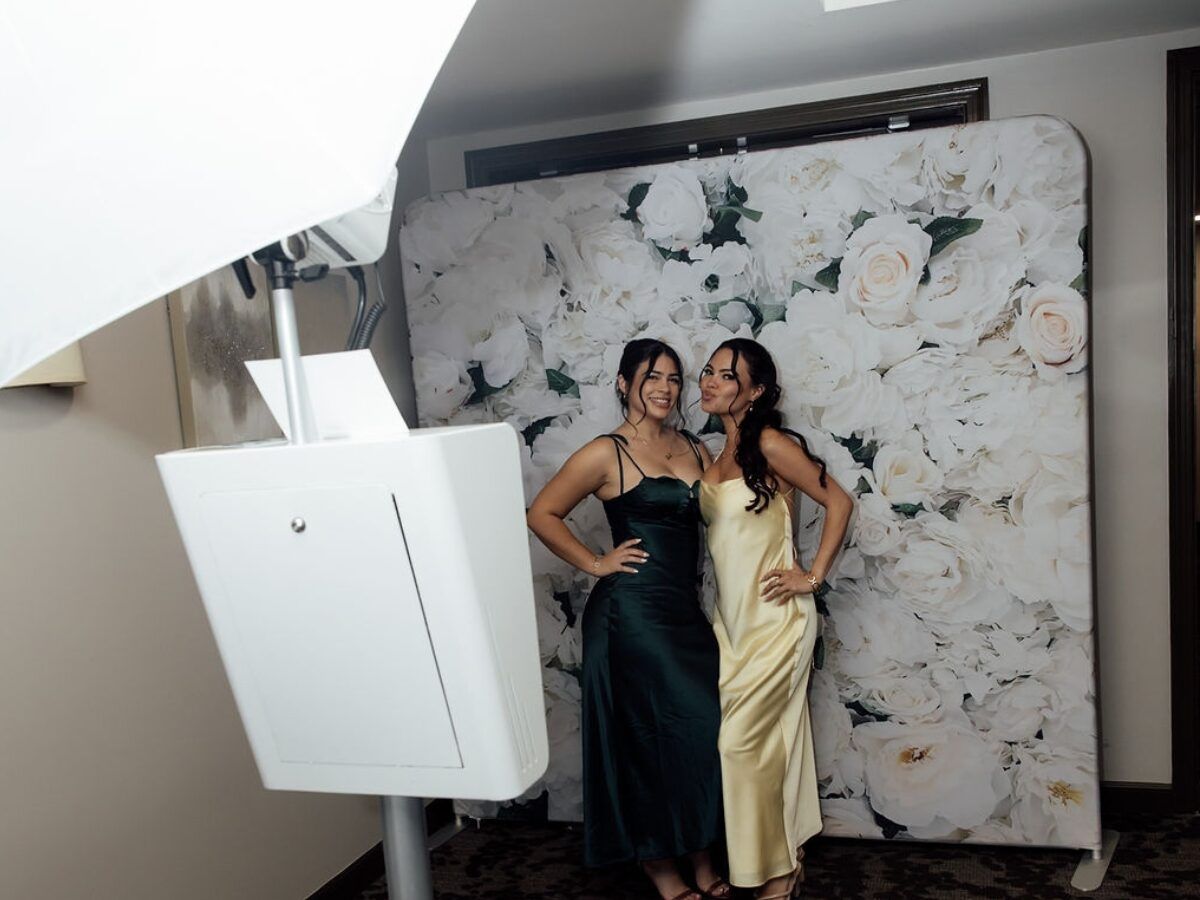 Guests posing at a photo booth set up against a white floral wall